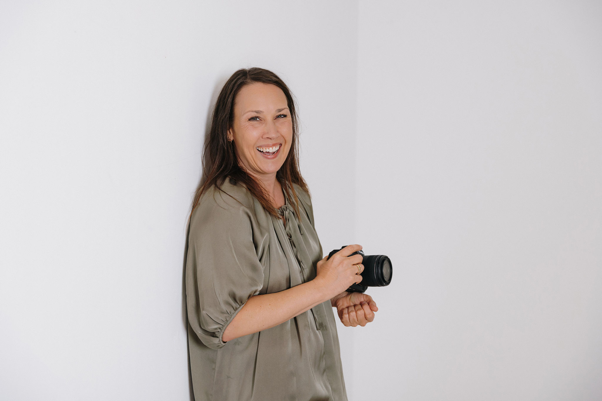 Personal Branding Fotografin Manuela Baum lächelt mit Kamera in der Hand ind die Kamera
